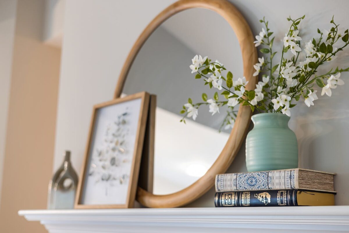 A stylish interior featuring a mirror, vase with flowers, and books on a shelf, creating a cozy ambiance.